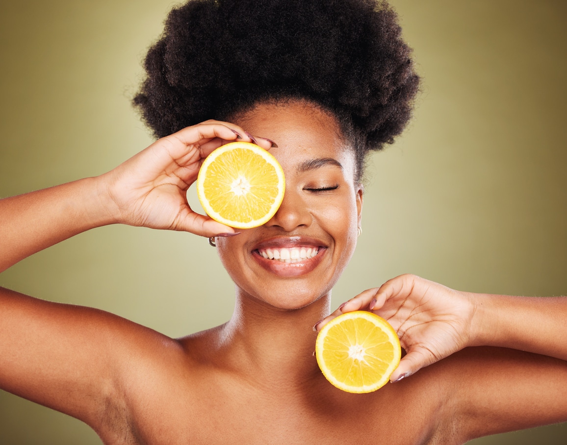 A lovely woman with a big smile positions lemon halves over her eye and her bare shoulder